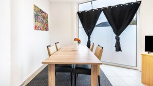 A modern meeting room with a wooden table, black chairs, a white vase with flowers, and a large window with black curtains.