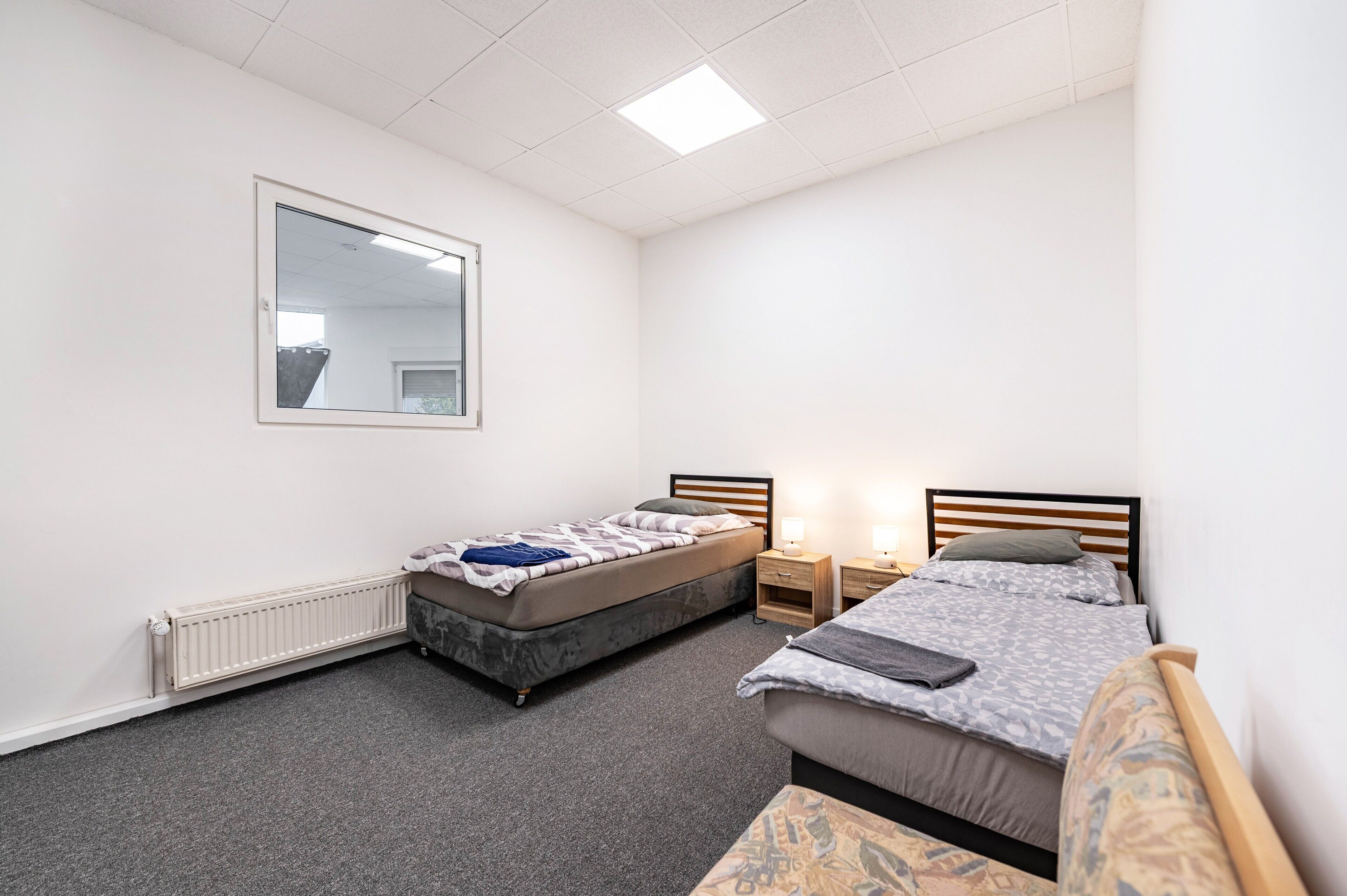 Een slaapkamer met twee bedden, een radiator, een spiegel en een raam.