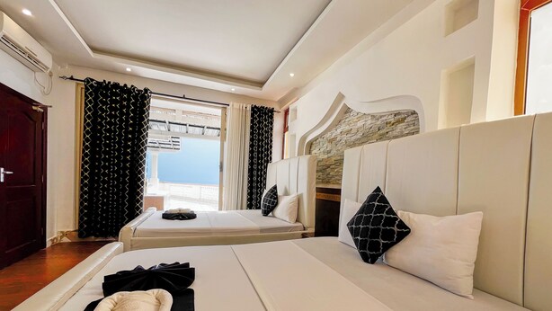 A hotel room with a large bed, a sofa, a window with curtains, and a stone accent wall. - Salt & Sun Sanctuary (Mombasa)