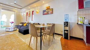 A modern living room with a sofa, dining table, and chairs, a kitchen with a water dispenser, and a large window with curtains. - Salt & Sun Sanctuary (Mombasa)