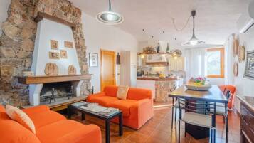 Un soggiorno con camino in pietra, divani arancioni, un tavolo da pranzo con sedie e una cucina sullo sfondo.