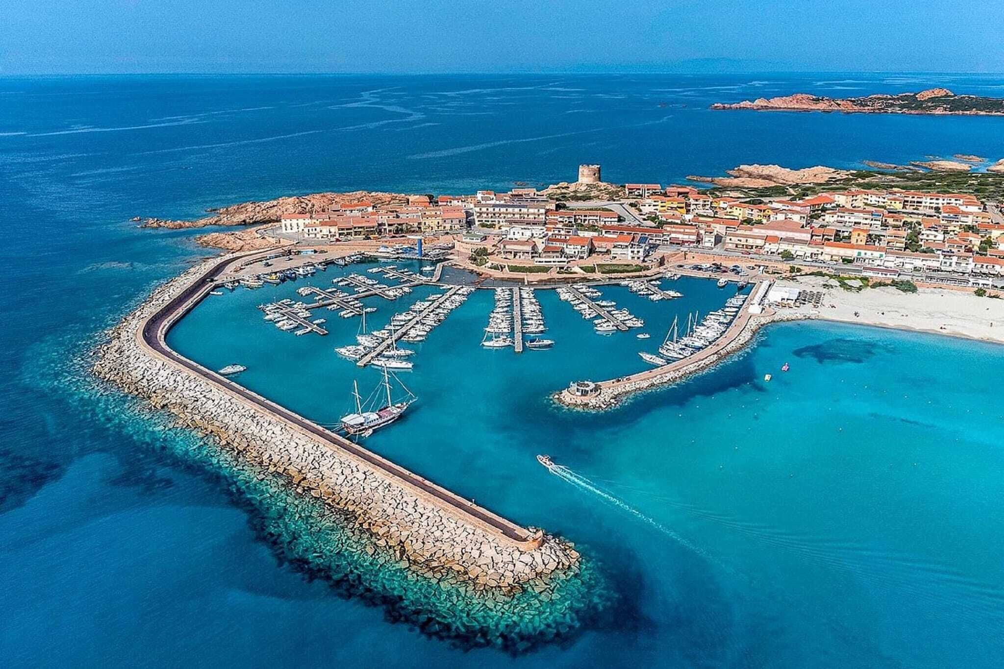 Vista aérea de un pueblo costero con un puerto deportivo, un puerto y una imponente estructura similar a un castillo.