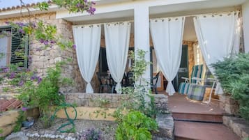 Una casa in pietra con un portico coperto, posti a sedere all'aperto e un giardino con diverse piante.