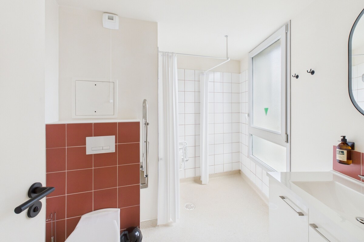 A modern bathroom with a toilet, sink, mirror, and shower.
