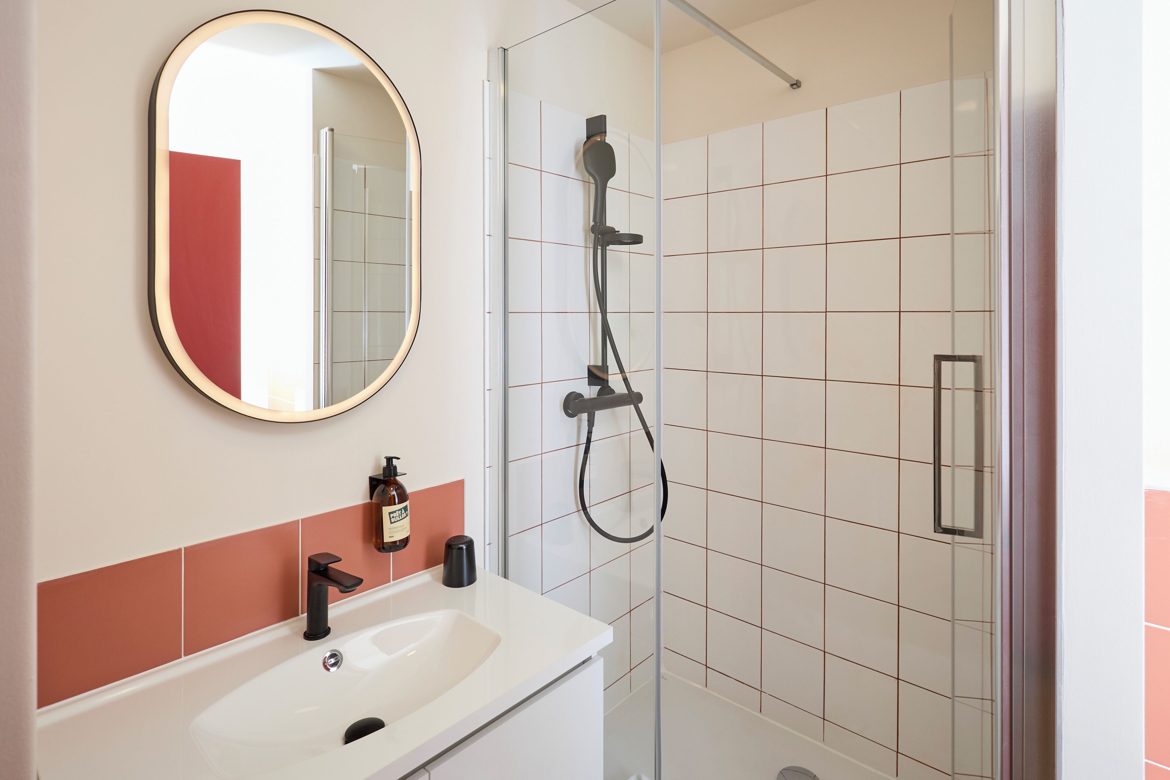 A bathroom with a white sink, a round mirror, and a glass-enclosed shower.