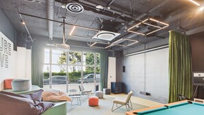 A modern indoor pool area with a pool table, seating, and a large window offering a view of the street.