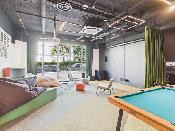 Un espace piscine intérieur moderne, doté d’une table de billard, de sièges et d’une grande fenêtre donnant sur la rue.