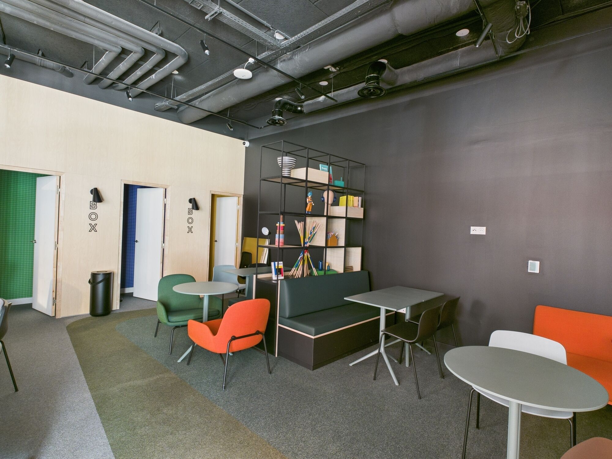 A modern lounge area with seating, a bookshelf, and a trash bin.
