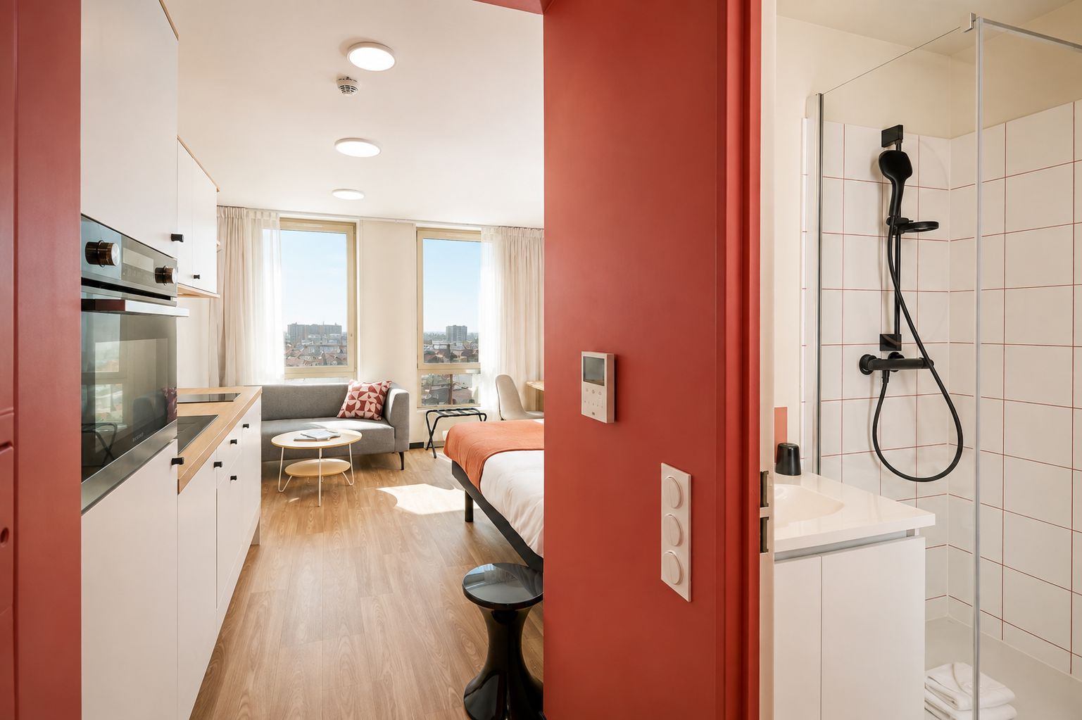 Une chambre d’hôtel moderne dotée d’une kitchenette, d’un coin salon avec un canapé et une table basse, d’un lit et d’un espace douche.