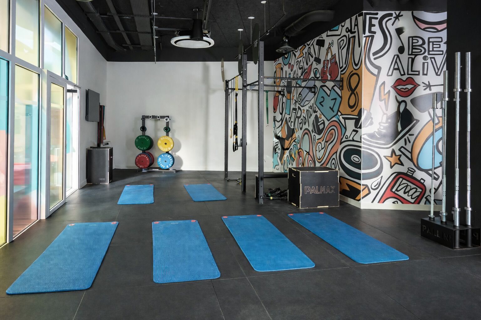 Un gimnàs amb estores blaves, equipament d'halterofília i un mural motivacional.