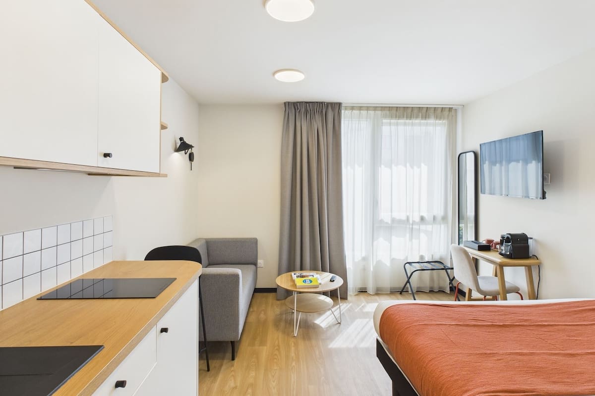Une chambre d’hôtel comprenant un lit, un bureau, une chaise, une petite table, un téléviseur et une fenêtre avec des rideaux.
