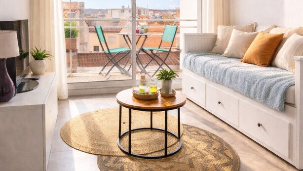 A modern living room with a large sliding glass door leading to an outdoor balcony, a round coffee table with decorative items, a sofa with cushions, and a hanging light fixture. - La Rose Des Vents - Studio - Arago - Sea View (Les Sables-d´Olonne)