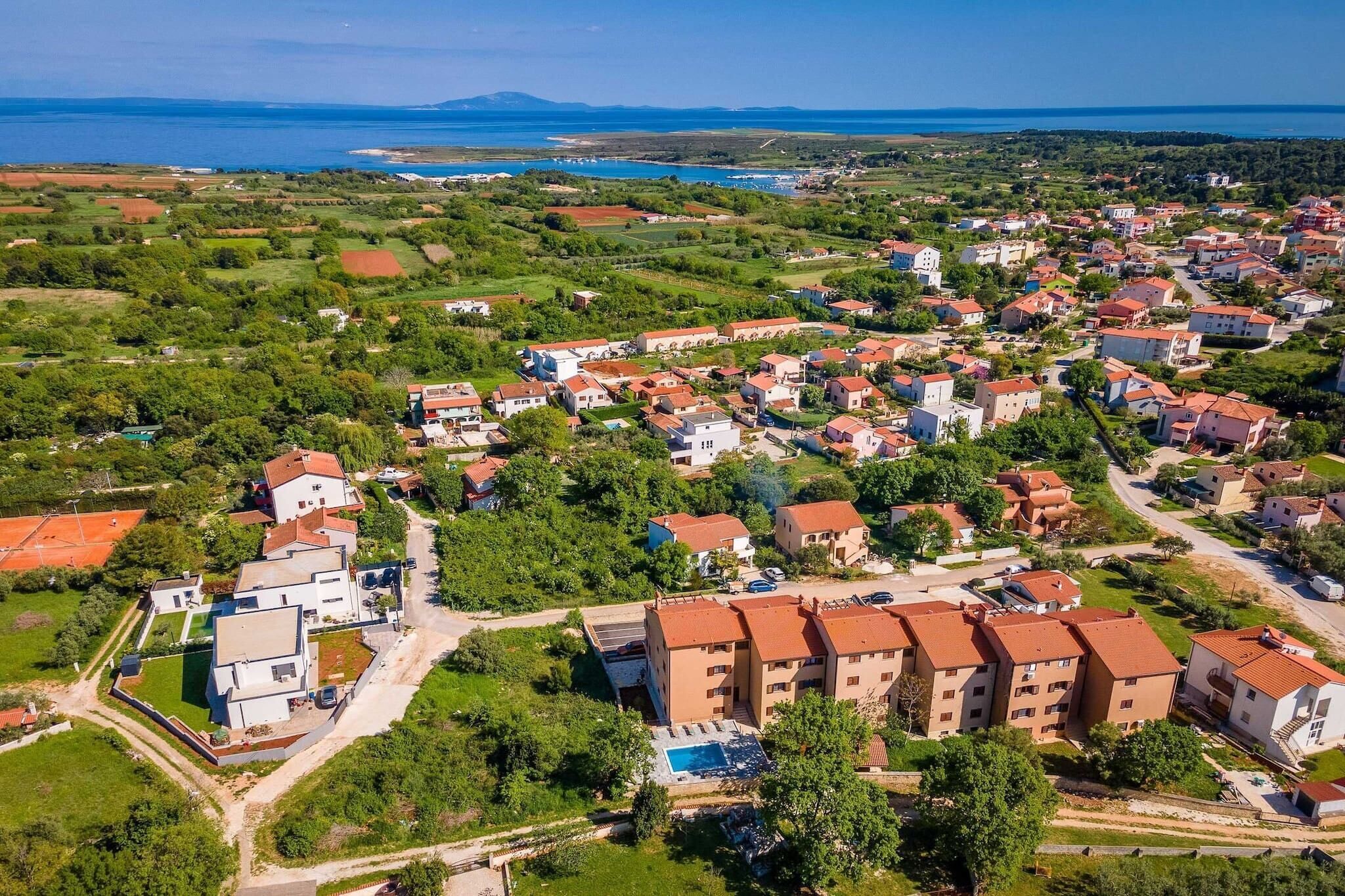 An aerial view of a residential area with houses, a swimming pool, and a view of the sea.
