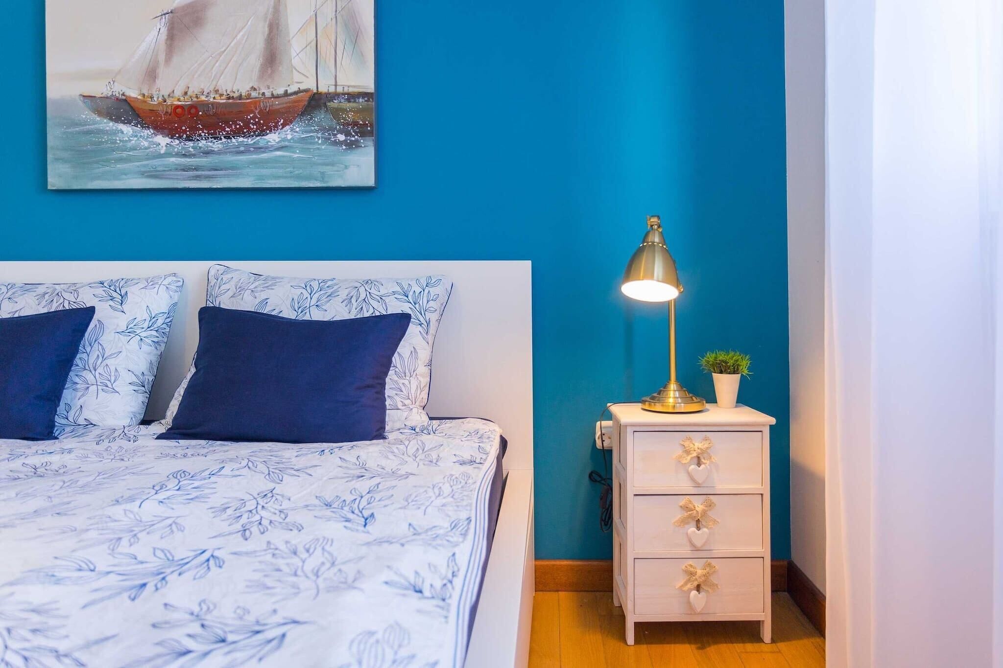 Quarto com cama, mesa de cabeceira, abajur e um quadro na parede.