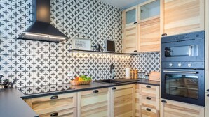 A modern kitchen with a black stove, wooden cabinets, and a backsplash with a geometric pattern. - 4 guests apartment in Medulin (Ližnjan)
