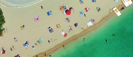 Vue aérienne d’une plage avec des personnes, des parasols et des chaises de plage.