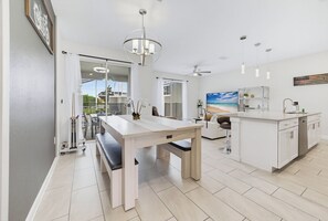 A modern kitchen with a dining area, a large window, and a ceiling fan.