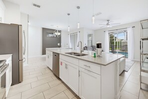 A modern kitchen with a central island, a built-in dishwasher, and a large window overlooking a pool.