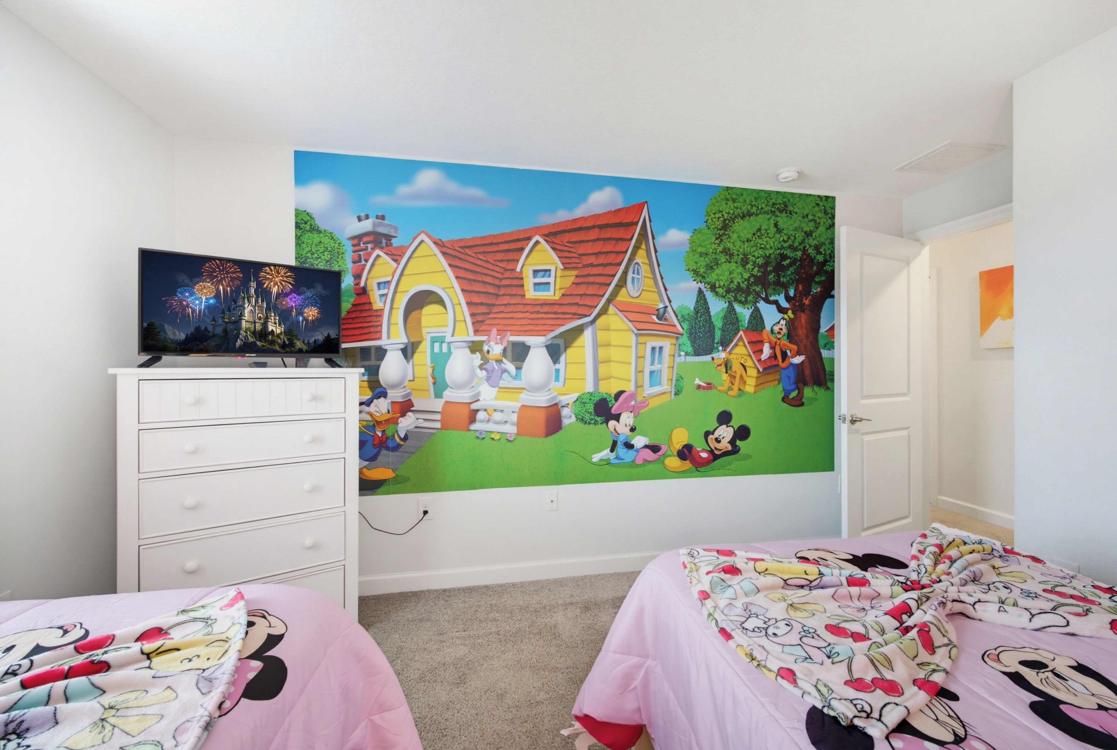A child's bedroom with a large wall mural, a TV, and two beds with Mickey Mouse bedding.