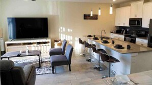 Una cocina moderna con una isla central, taburetes de bar, un televisor de pantalla plana y un ventilador de techo.
