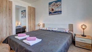A bedroom with a large bed, a bedside table with a lamp, a mirror, and a painting on the wall.