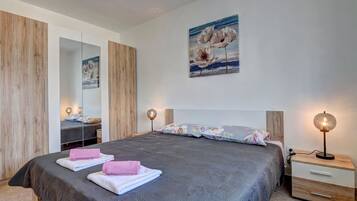 A bedroom with a large bed, a bedside table with a lamp, a mirror, and a painting on the wall.