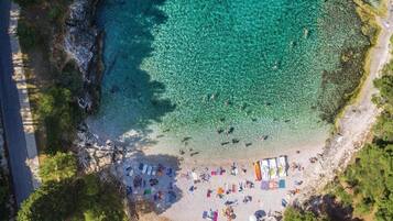 An aerial view of a beach with clear turquoise water, a sandy shore, and several colorful umbrellas and beach chairs.