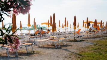 A beach with rows of sun loungers and umbrellas, some occupied, others empty.