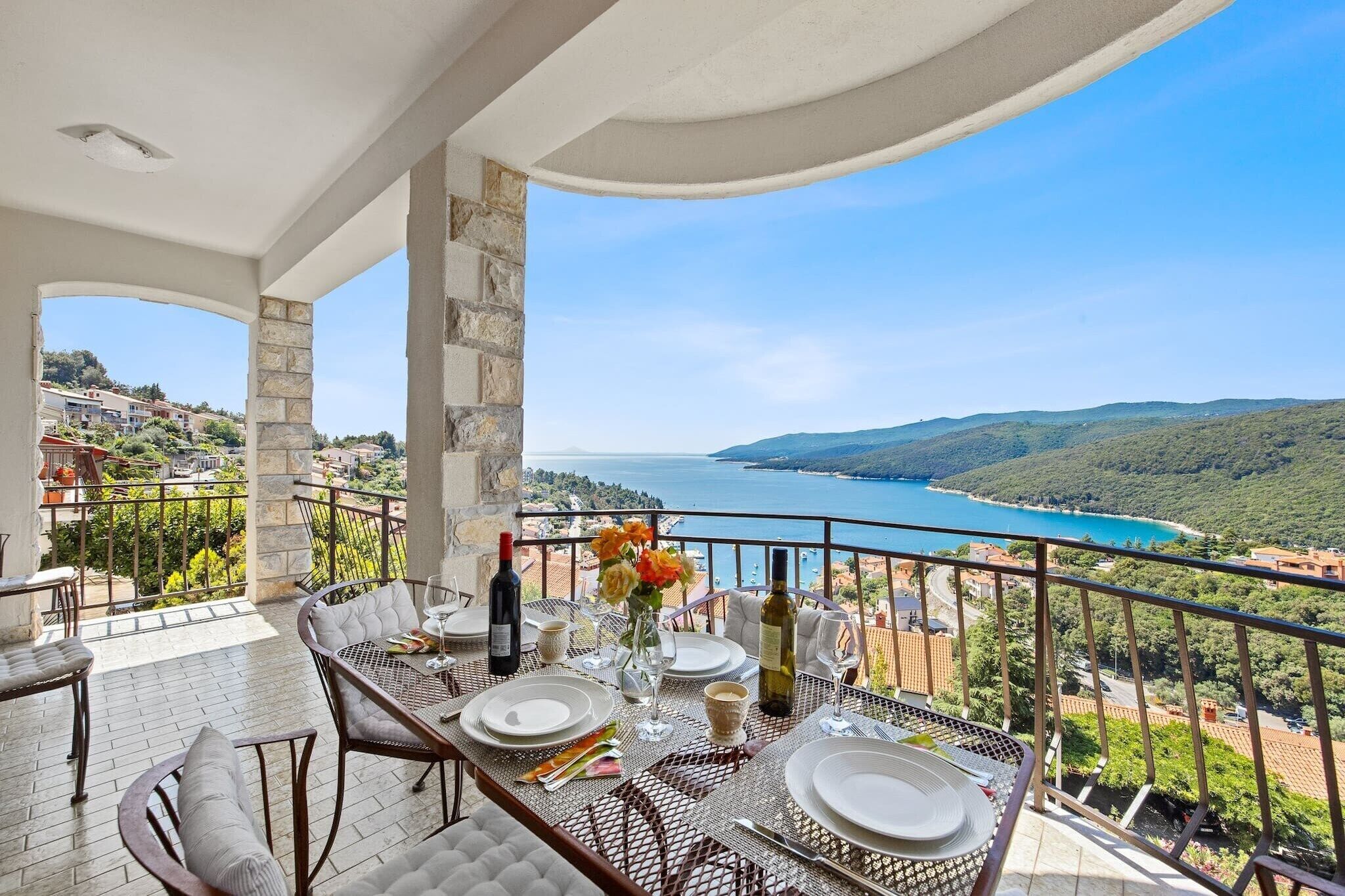 A balcony with a table set for dining, overlooking a scenic coastal view.