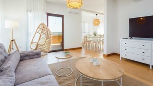 A modern living room with a sofa, a round coffee table, a hanging chair, a TV, and a dining area in the background.