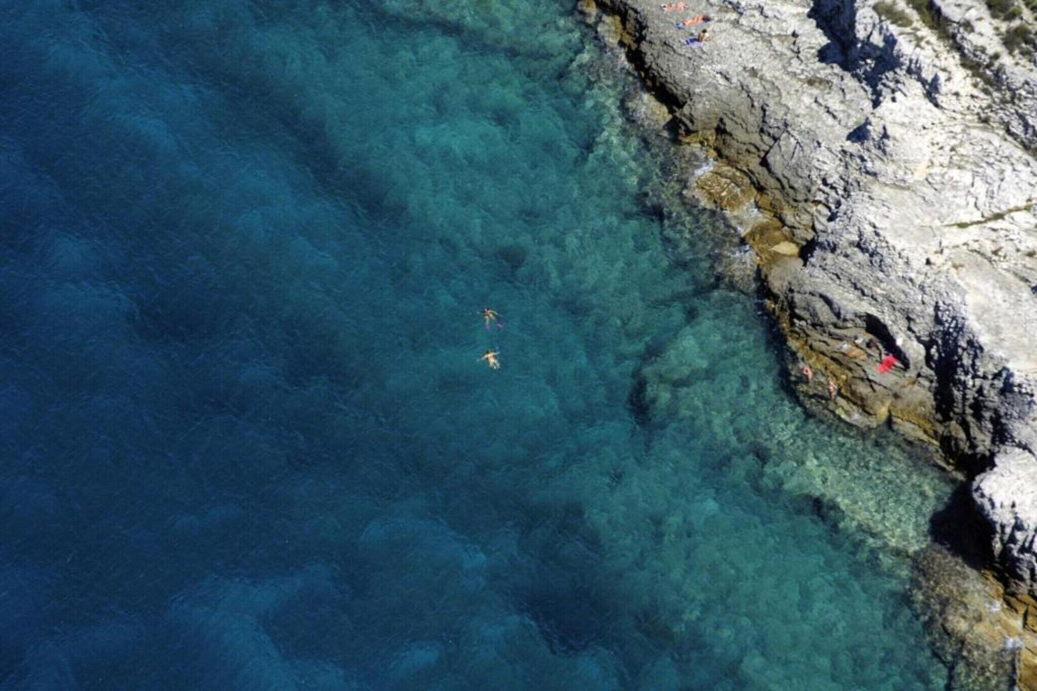 A coastal area with clear water, rocky terrain, and people swimming.