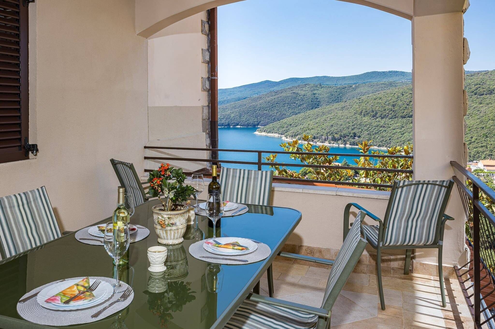 A balcony with a table set for two, overlooking a scenic view of a lake and mountains.