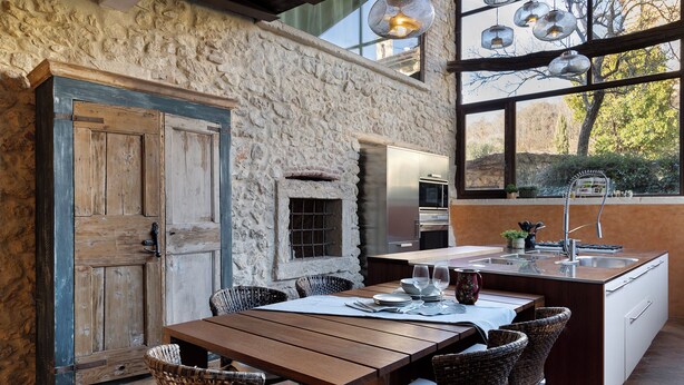 Une cuisine rustique avec un mur en pierre, des armoires en bois et un grand îlot central doté de tabourets de bar.