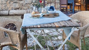 Un espace extérieur aménagé avec un mur en pierre, une table en bois, des chaises en osier et une vue sur un espace intérieur.