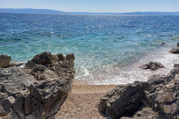 A rocky shoreline with clear blue water and distant mountains.