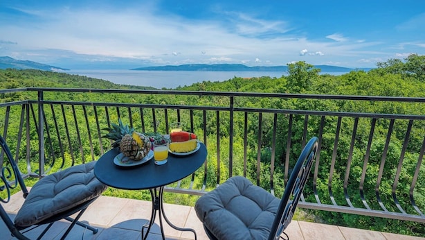 A balcony with a table set for breakfast, featuring a pineapple, watermelon, and orange juice.