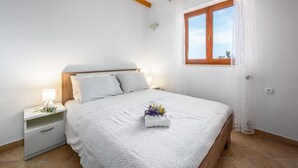 A bedroom with a bed, a nightstand, a window with curtains, and a wooden ceiling beam. - Apartment in Drenje with Stunning Sea View (Drenje)