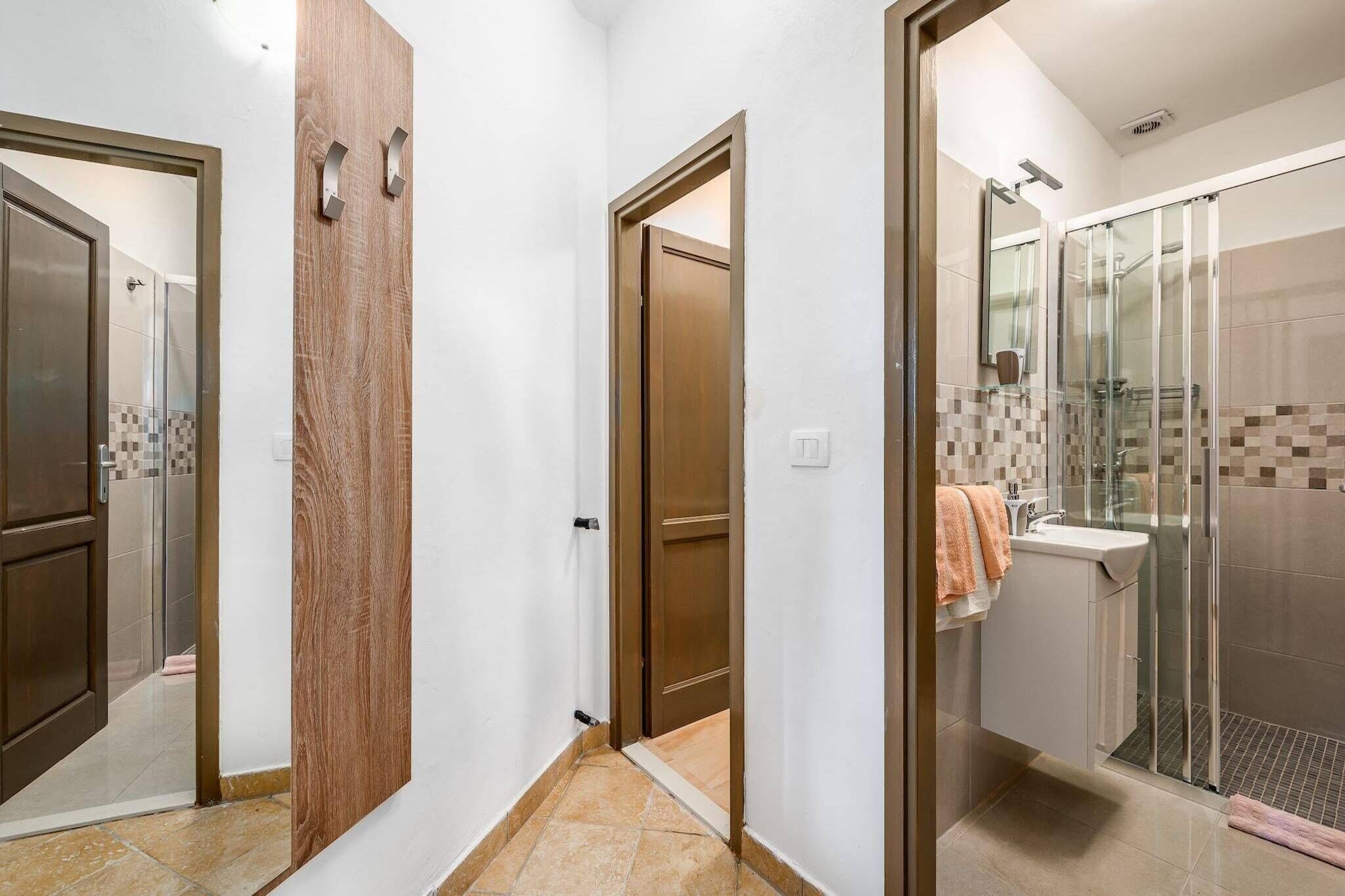 A hallway leading to a bathroom with a glass shower enclosure, a sink, and a wooden door.