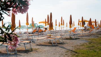 A beach with rows of sun loungers and umbrellas, some occupied, others empty.