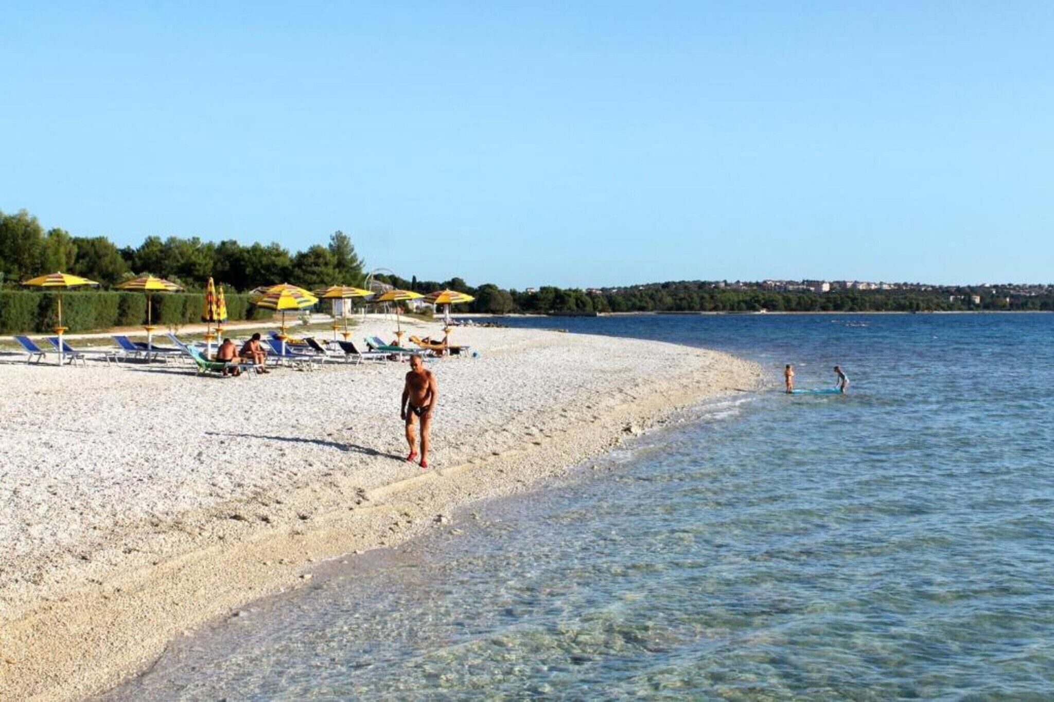A beach with sun loungers and umbrellas, a clear sky, and a calm sea.