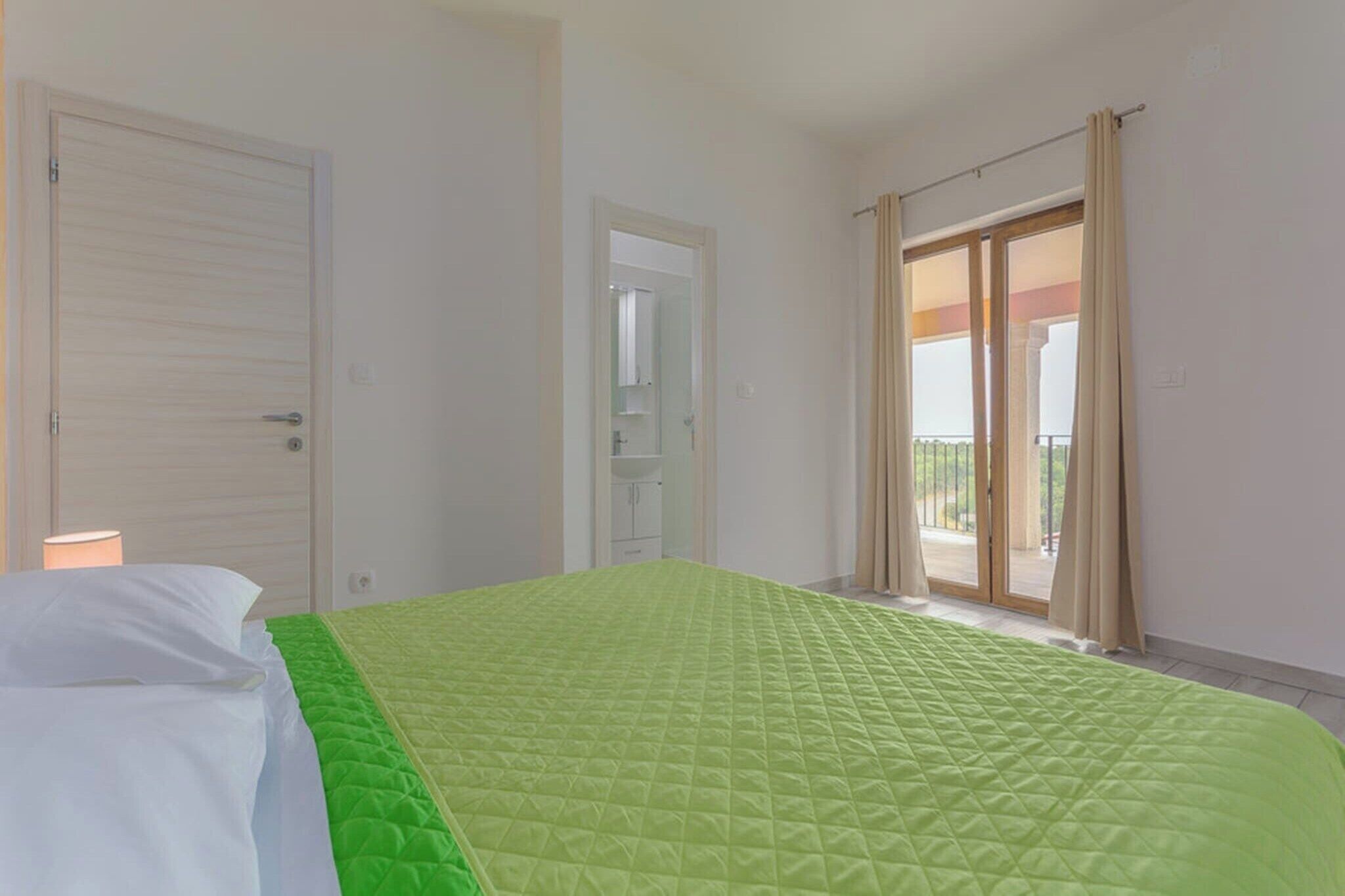 Une chambre d’hôtel avec un lit, une porte, une salle de bain et un balcon avec des rideaux.