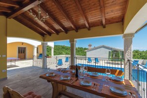 A covered outdoor dining area with a table set for two, overlooking a swimming pool and a building with a stone facade. - Villa in Skitaca with Pool and Sea Views (Koromačno)