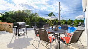 A patio with a grill, table, chairs, and a pool. - Spacious Apartment in Markoci (Markoci)