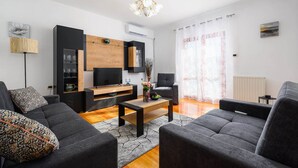 A modern living room with a flat-screen TV, grey sofas, a wooden coffee table, and a chandelier. - Spacious Apartment in Markoci (Markoci)