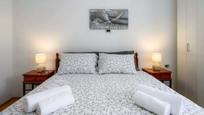 A neatly made bed with floral bedding, two bedside lamps, and a wall-mounted artwork. - Spacious Apartment in Markoci (Markoci)