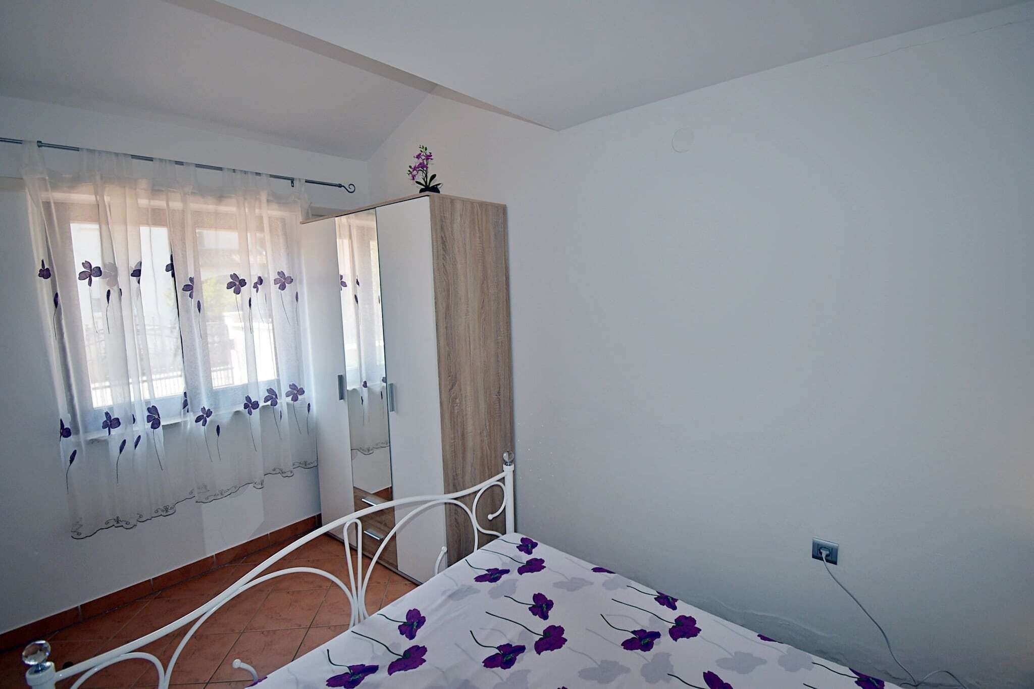 A bedroom with a bed, a window with sheer curtains, a wooden wardrobe, and a white metal bed frame.