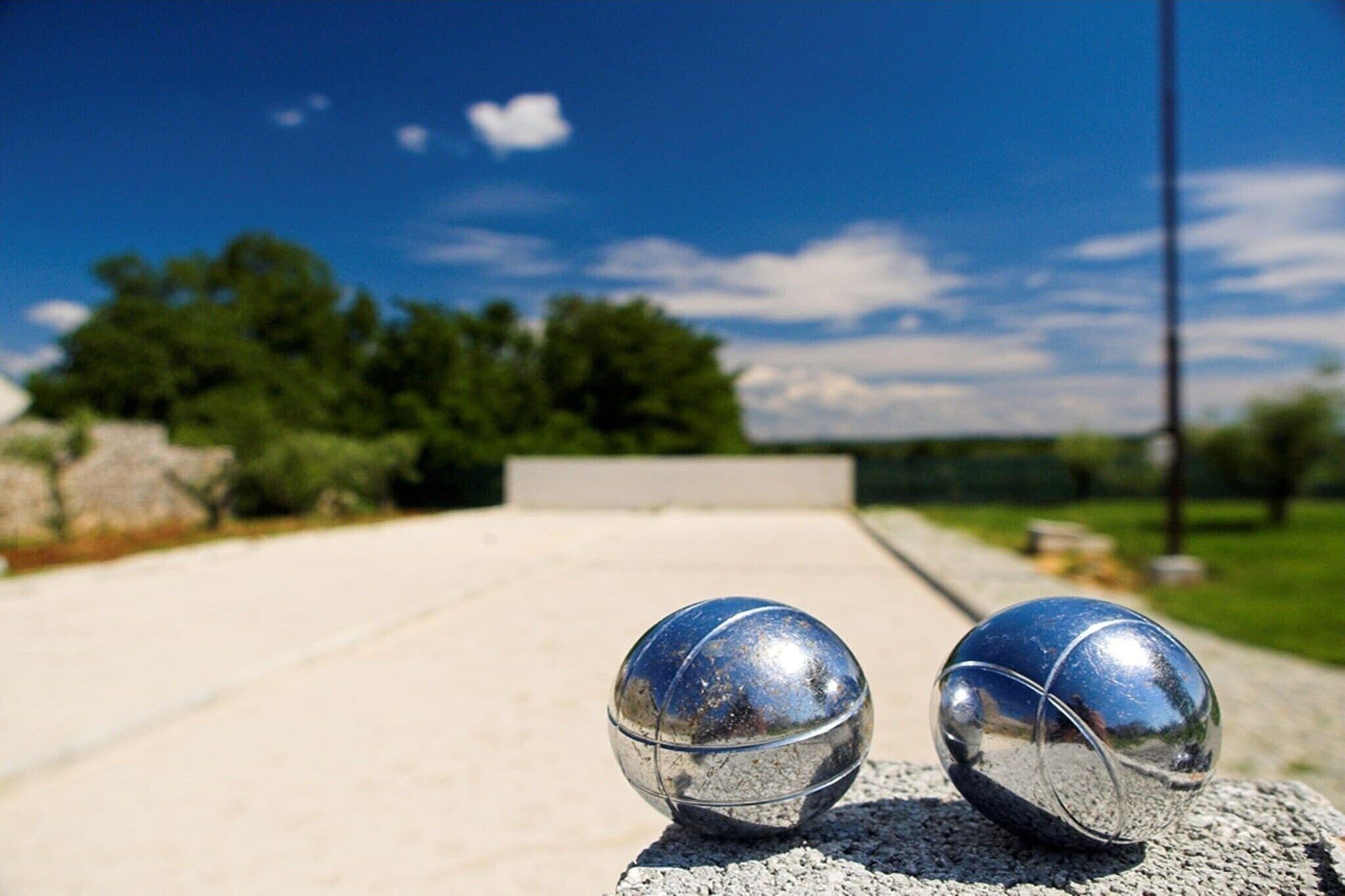 Two metallic spheres on a concrete surface with a clear sky and greenery in the background.