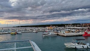 A marina with boats docked, a pier with people, and buildings in the background.