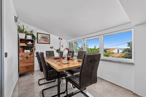 Een eethoek met een houten tafel, zwarte stoelen, een potplant en een schilderij aan de muur.
