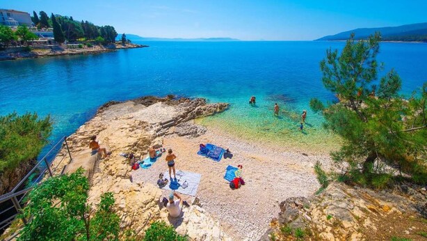 A coastal beach with clear water, rocky shore, and people sunbathing. - Cozy Apartment Near Beach (Rabac)